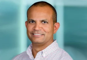 Professional headshot of a smiling male business professional wearing a checkered shirt